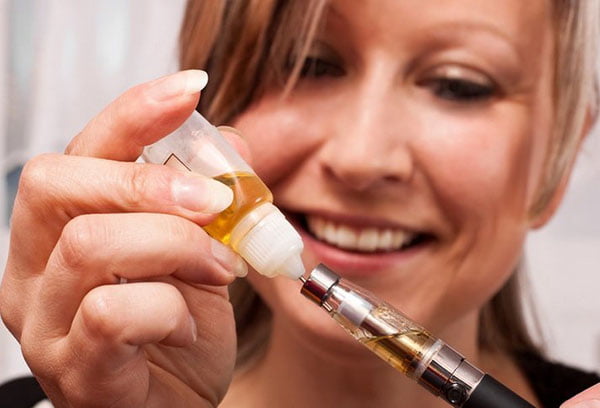 Женщина заправляет вейп